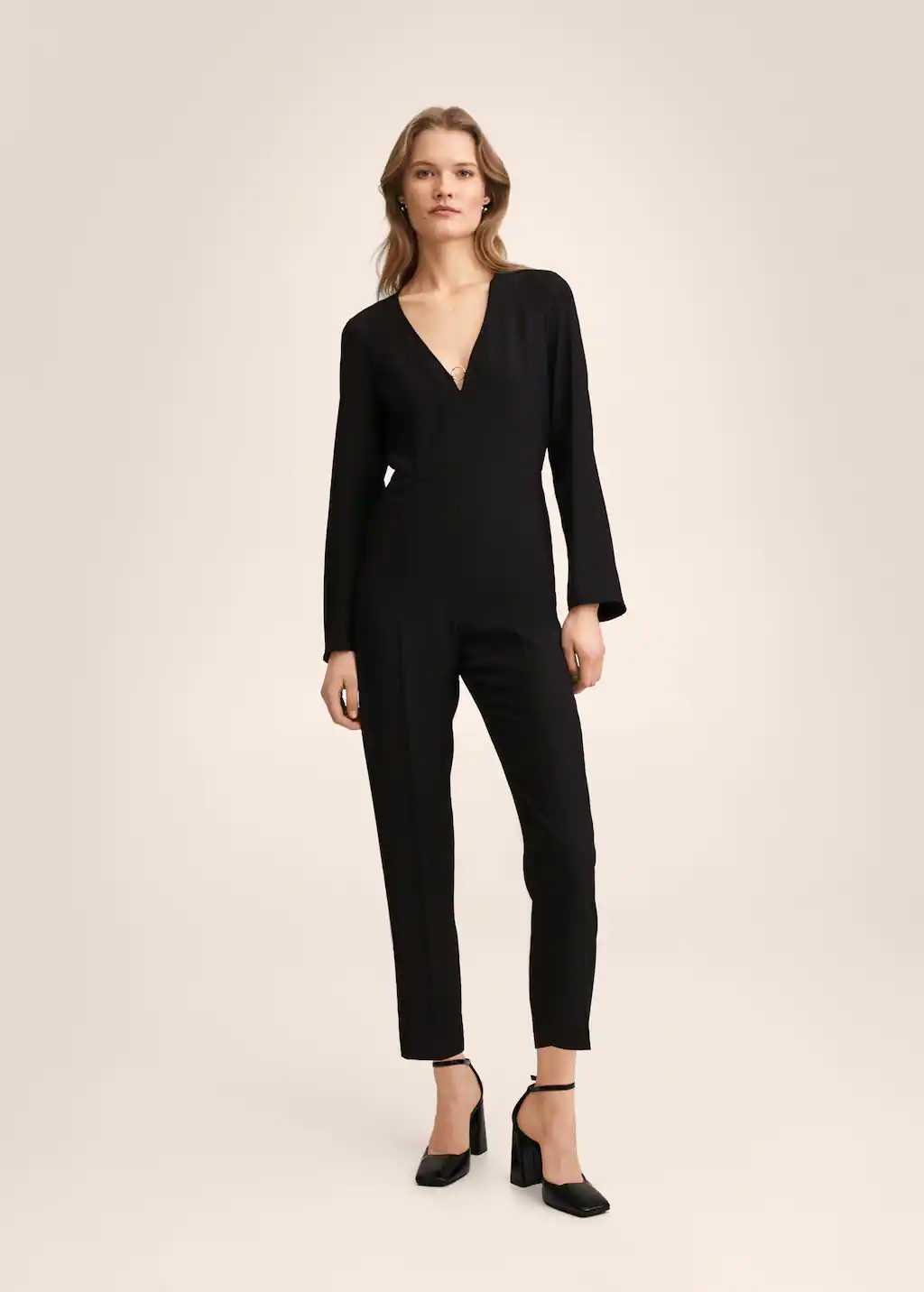 Full length black fluid jumpsuit with long sleeves and v neck featuring metal ring detail. Zip closure and two side pockets. 
