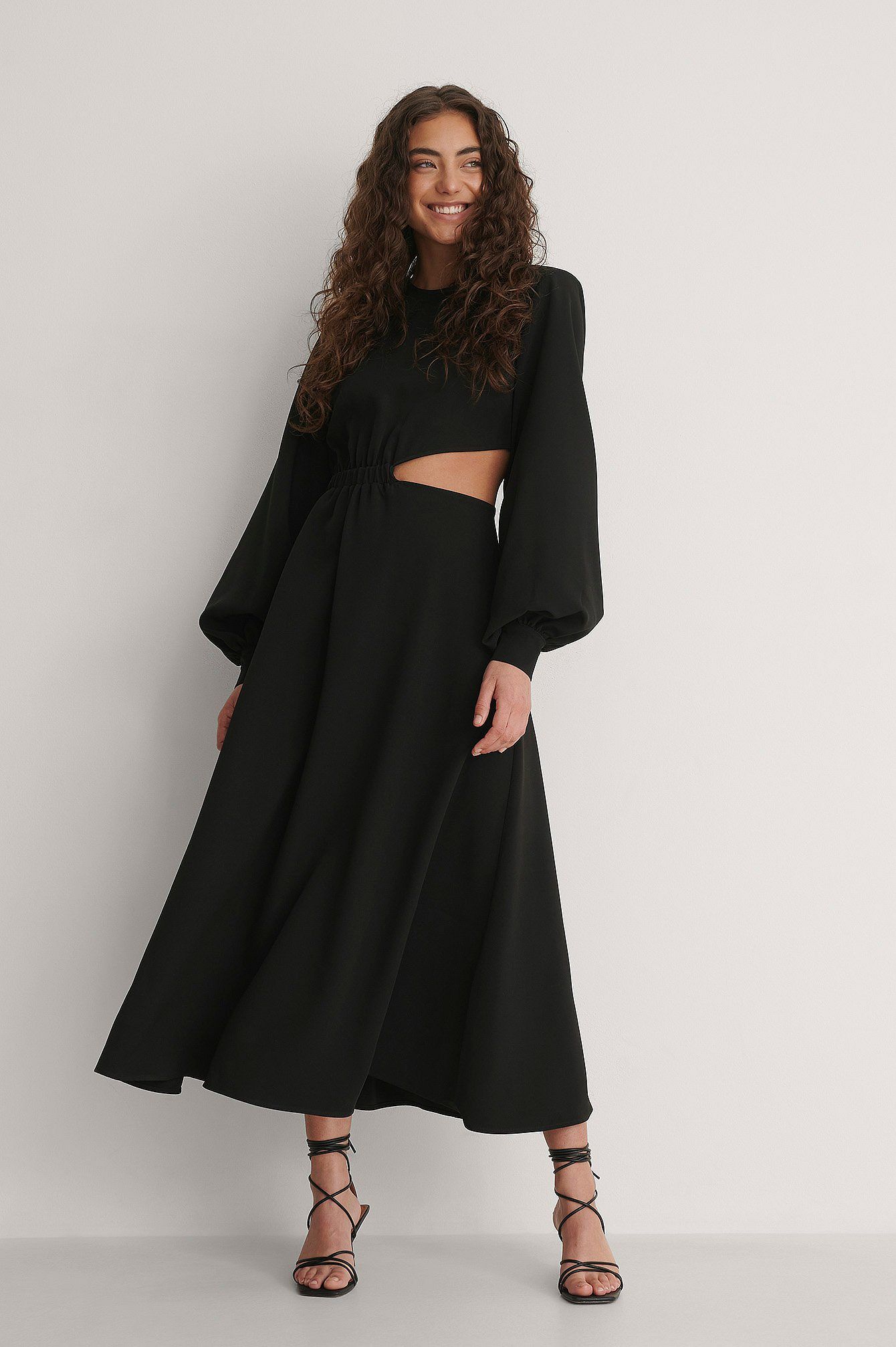 Black Midi dress with long full sleeves that taper at the wrist. Round neck and nipped in waist with a side cut out over the waist revealing a little skin. 