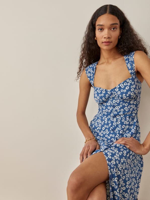 The Tayler is a midi length dress with a sweetheart neckline. It features a button front and ties at the back neck. It has a smocked back bodice for a little bit of stretch and wide straps. Blue base with white ditsy floral print.