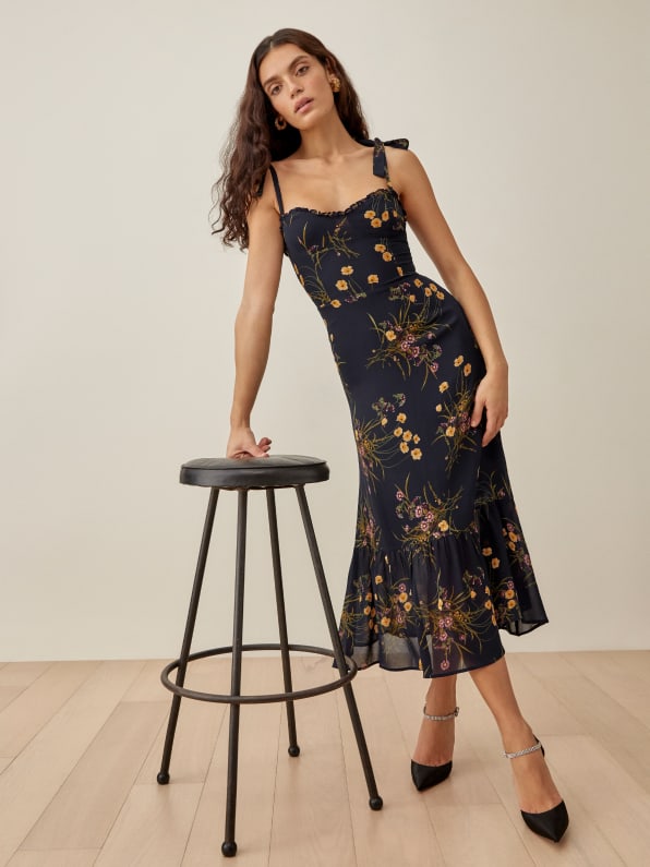 The Nikita is fitted in the bodice and waist with a relaxed fitting skirt. This midi length dress has a ruffle edged neckline, adjustable strap ties, and a trumpet skirt. It gives you a pretty good balance of comfort and shape.