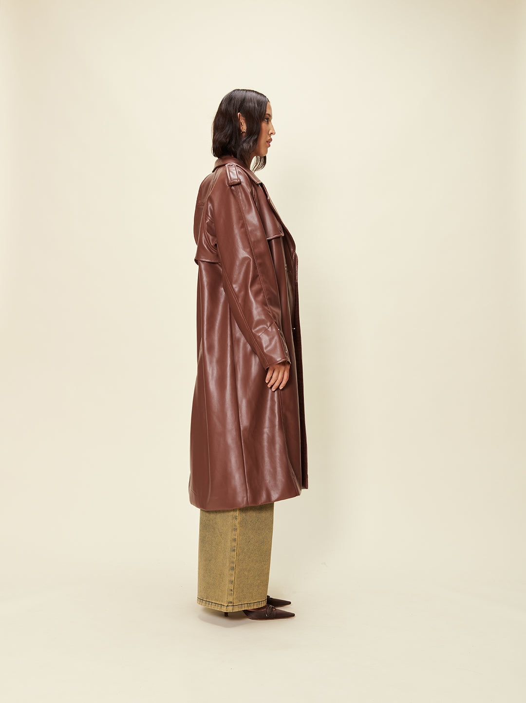House of sunny chocolate brown leather trench coat in faux leather. Classic trench coat silhouette in Custom brown HoS colour scheme. It has a Retro collar, Double breasted buttoning, Long line fit, Vegan leather fabric.  Side welt pocket detailing. 