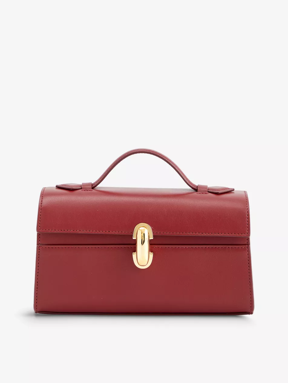 SAVETTE Symmetry Pochette leather top-handle bag in dark red wine colour. Structured shape, top handle, brand text print under flap, one main compartment, grain texture, gold-toned hardware