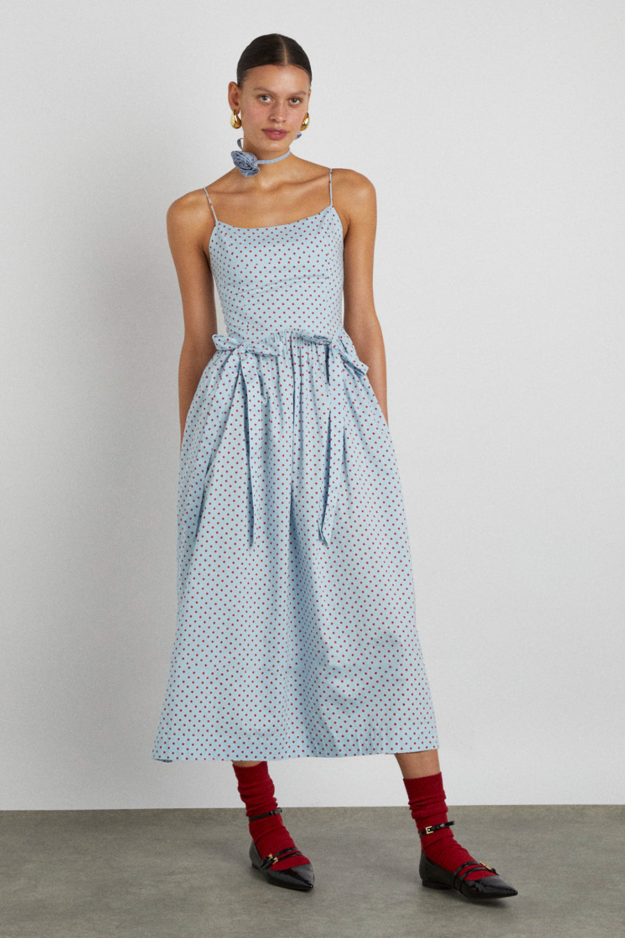 The Damson madder Penelope apron dress is our light blue and red polka dot midi dress featuring a corset style bodice with waist seam details and bows that gather into a fuller skirt.    